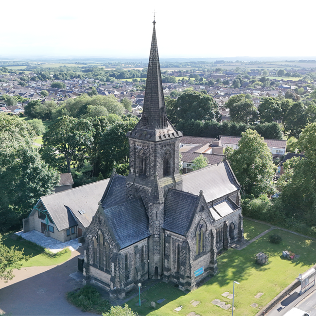 A historic white church with a tall, pointed steeple topped by a weather vane, surrounded by a graveyard with aged, moss-covered headstones. The church features arched stained glass windows, brick acc