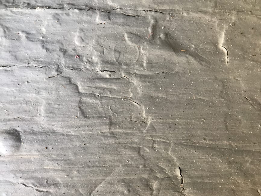 Close-up image of a wooden surface with visible cracks, scratches, and uneven texture, showing signs of wear and damage. The surface appears aged, with dull coloration and some dust particles present.